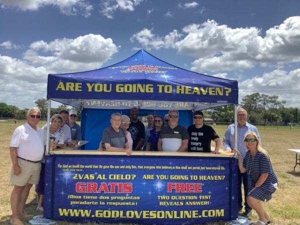 A group of people standing around a fair booth that reads, "Will you go to heaven?"